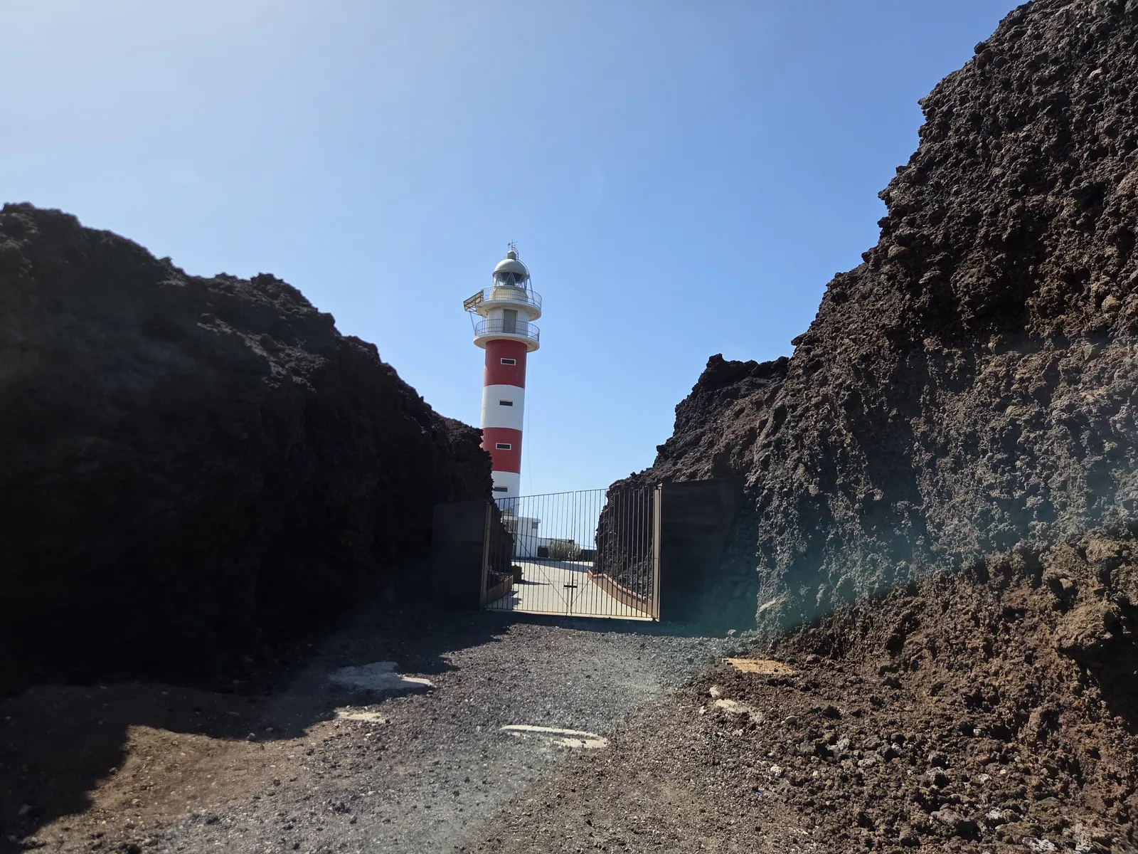 Faro rojo y blanco de Punta de Teno visto entre paredes de roca volcánica